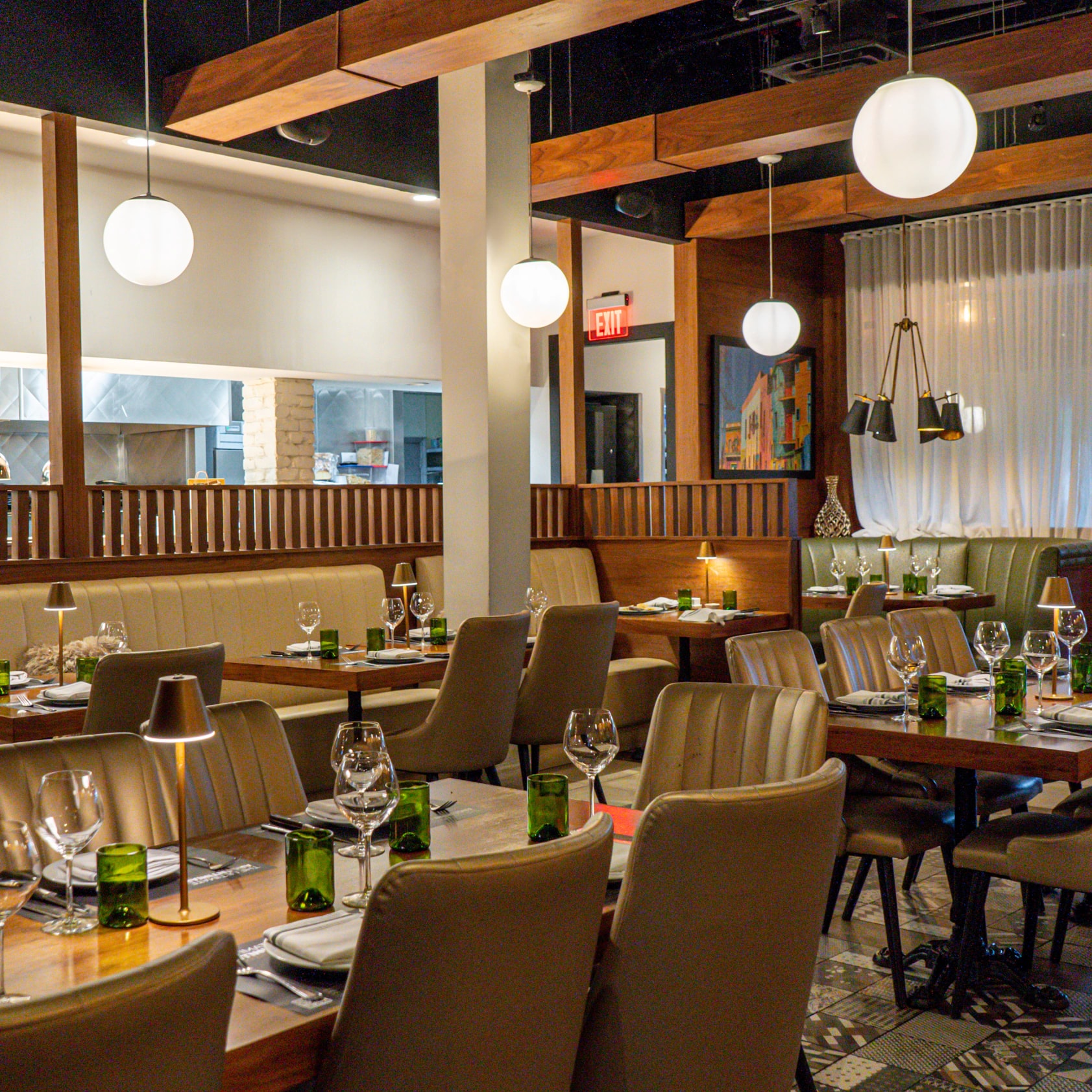 The Baires Grill Weston dining room, tables set under globe pendants with leather booths and a sheer curtain