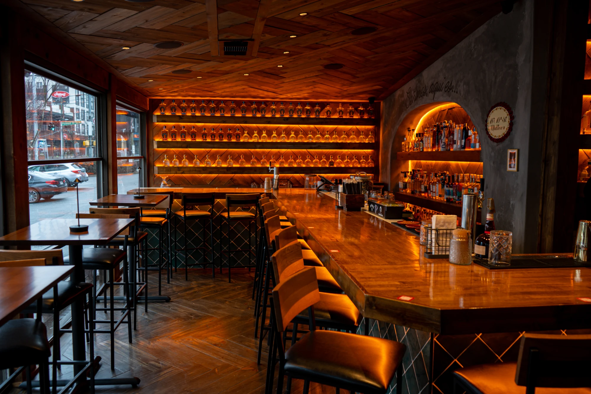 The bar at Zócalo, amber-lit shelves of tequila over a long wooden counter with the Midtown street outside