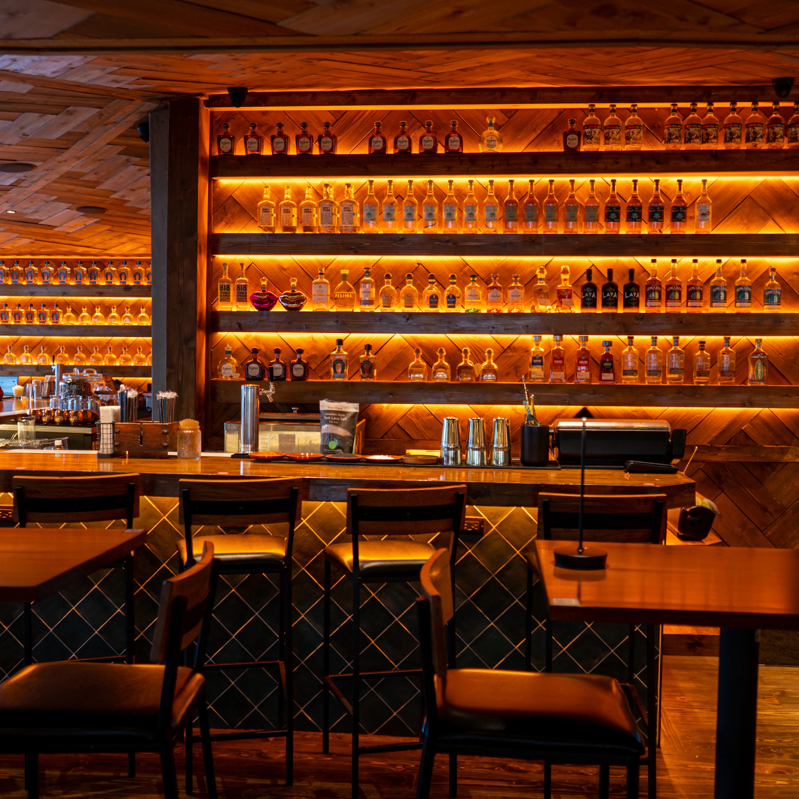 The back bar at Zócalo, amber backlit shelves of tequila above a tiled bar front and a row of high stools